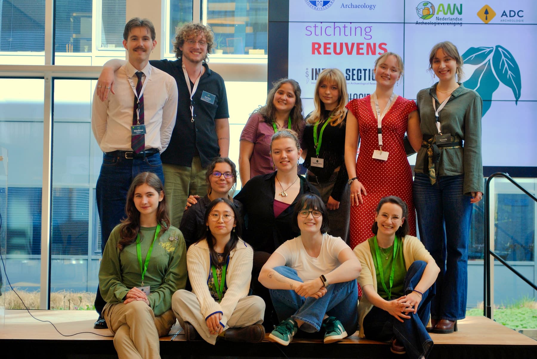 A group of young archaeologists smiling together on stage after SoYA 2026, with sponsor logos and the SoYA logo displayed on screens behind them